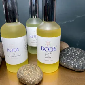 Three skincare bottles labeled 'BODY' with smooth stones on a dark surface.