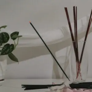 Glass containers holding incense sticks against a light wall.